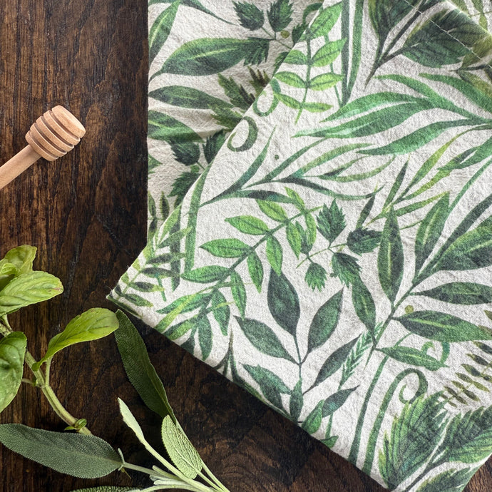 Green leaf-patterned fabric on a wooden surface with fresh green leaves.